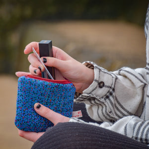 Close up of hands taking a lipstick and credit card out of a handmade purse in blue tweed fabric.