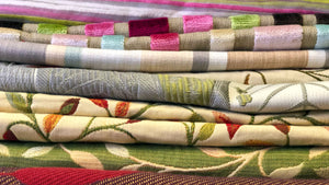 Close up of a stack of upcycled fabrics in the ReTweed workoom. A selection of patterns and designs including pink, green and brown stripes and green and red florals.
