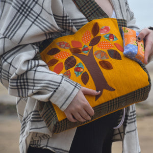 Close up of a young woman holding a handmade bag. The bag is tweed with an orange applique panel with a tree.