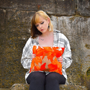 Young woman sitting on a wall holding a handmade cushion. The cushion is a bright orange with red, white and beige