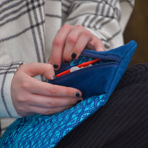 Close up of hand opening a roll top cosmetic bag to reveal the contents. An indigo blue fabric with a blue and turquoise patterned inside