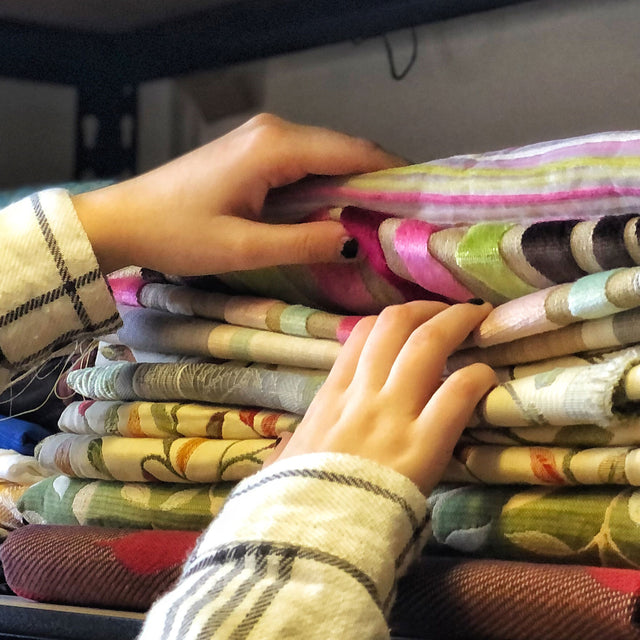 Close up of someones hands selecting fabric from a shelf in the ReTweed workroom