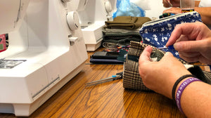 Close up of hands stitching a section of Tweed fabric in the workroom next to a sewing machine.