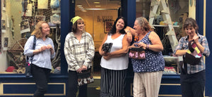 Retweed folk outside the Retweed shop in Eyemouth. They are chatting and laughing together, as they hold handmade items from the shop