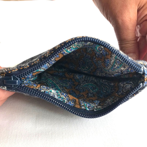 The inside of blue and grey tweed purse with blue, green and beige paisley patterned fabric